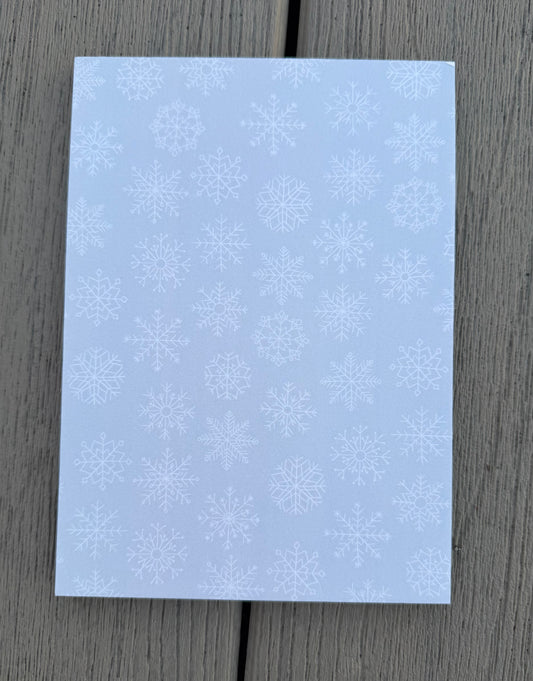 Blue 5x7 snowflake notepad with delicate white snowflake pattern on a gray wooden background.